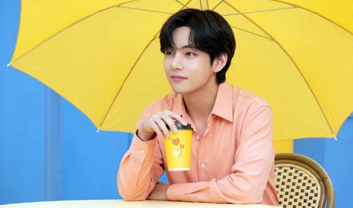 Person with coffee under yellow umbrella