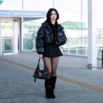 aespa Karina's iconic airport fashion featuring a glossy black puffer jacket and tall boots.